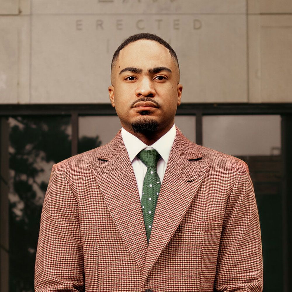 Lorenzo Smith in plaid suit and green tie standing confidently in front of a building.