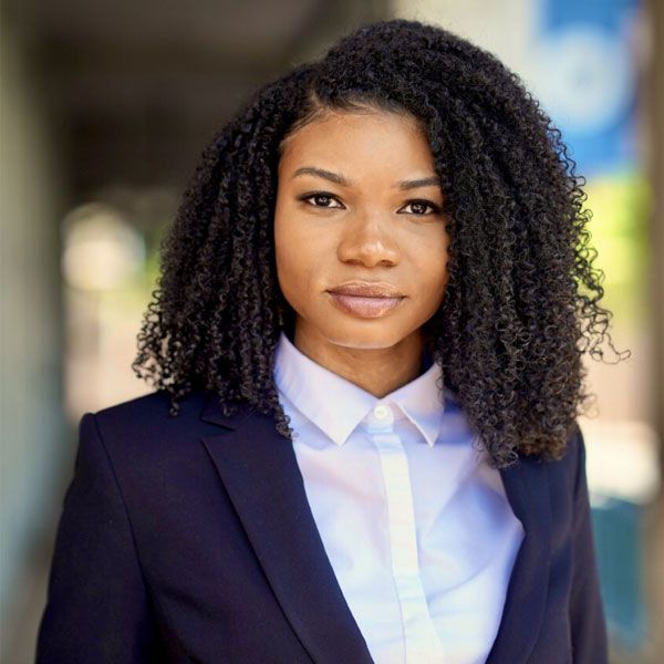 Brittany Larcart with curly hair in a navy suit, confidently looking forward in an outdoor setting.