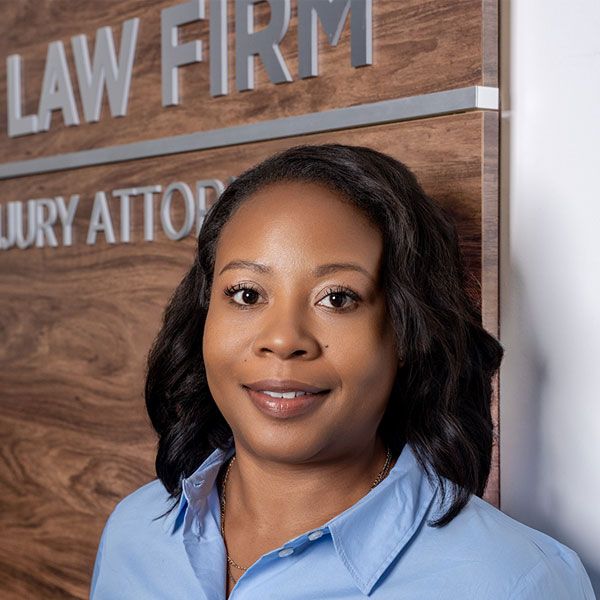Portrait of a professional woman in front of a law firm sign, wearing a blue shirt.