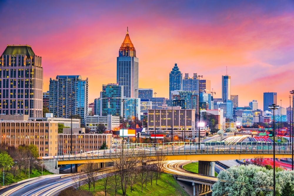 Atlanta skyline at sunset with vibrant skies and modern skyscrapers, busy roads with light trails in the foreground.