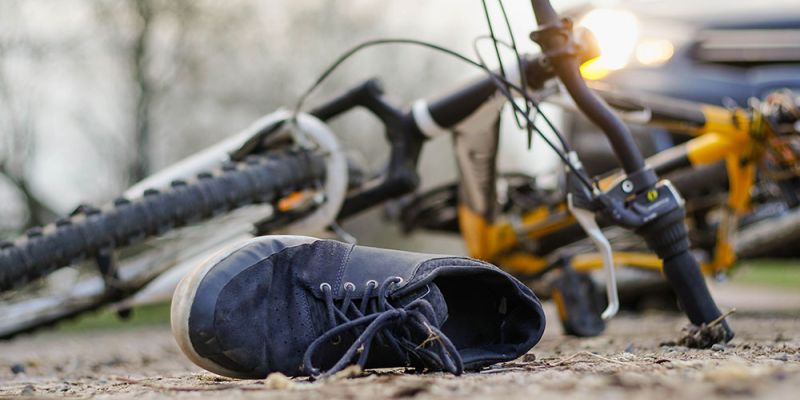 Bicycle accident scene, shoe on ground, bike overturned near car with headlights on, emphasizing road safety awareness.