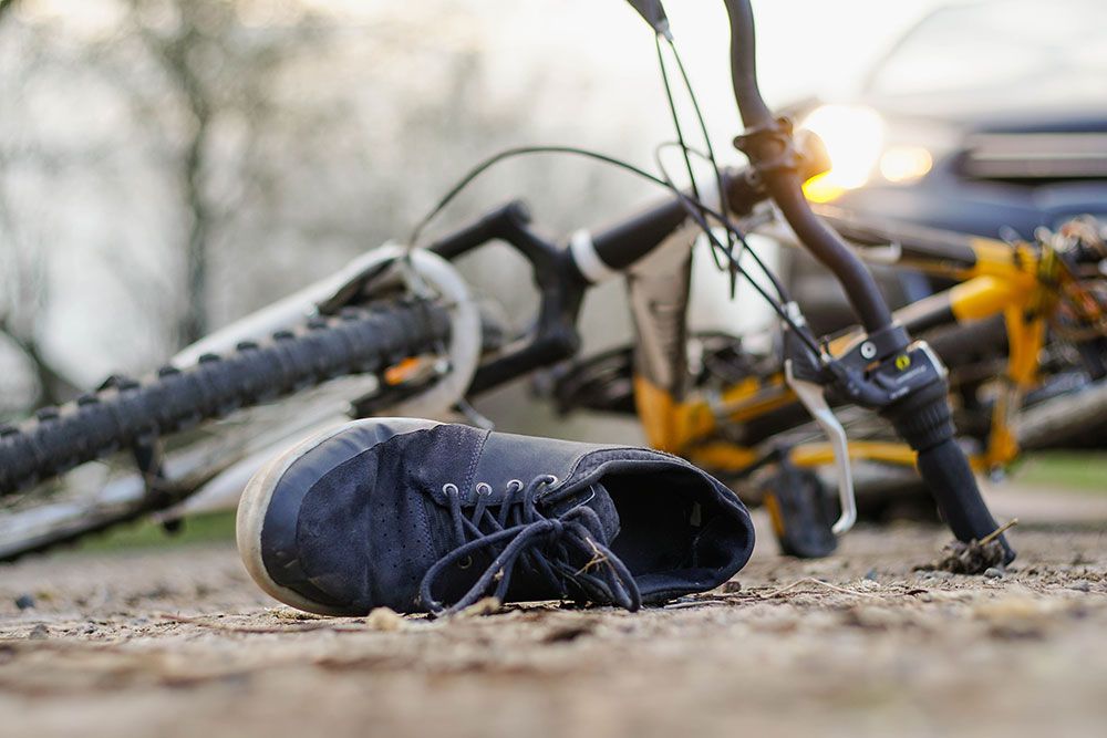 Bicycle accident scene, shoe on ground, bike overturned near car with headlights on, emphasizing road safety awareness.
