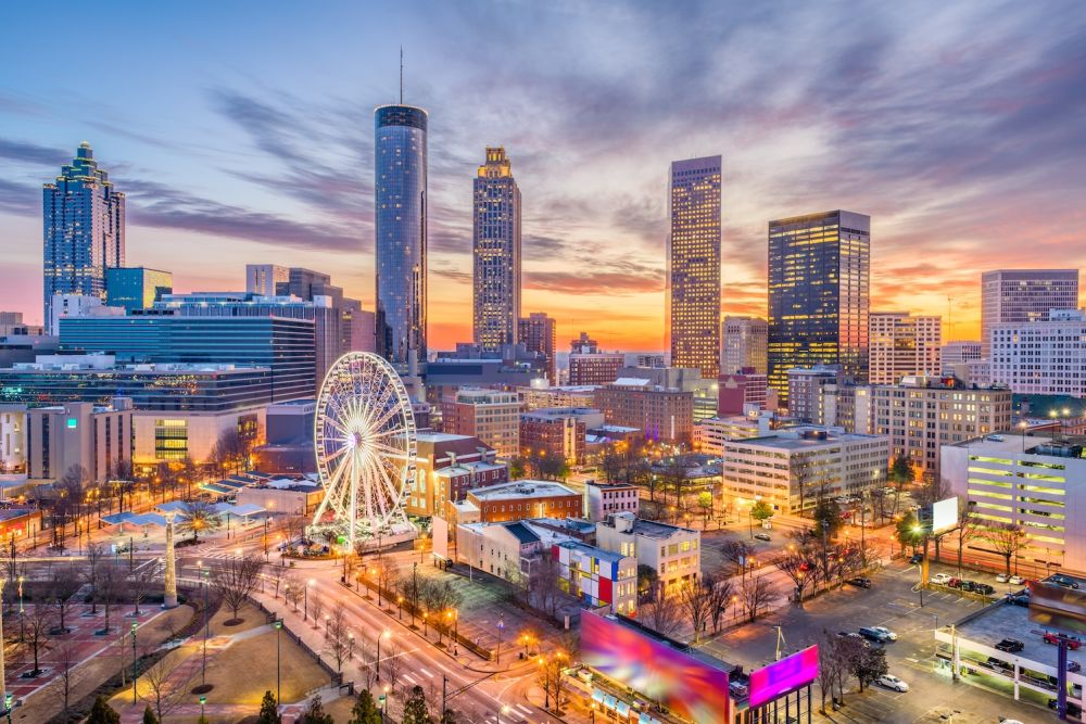 Atlanta skyline at sunset with Ferris wheel and skyscrapers, showcasing vibrant city life and urban architecture.